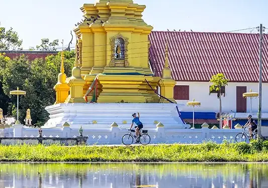 A cyclist waving in front of a Thai temple. (c)Backroads