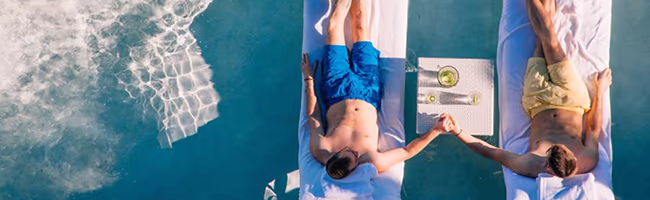 Two men hold hands on pool loungers